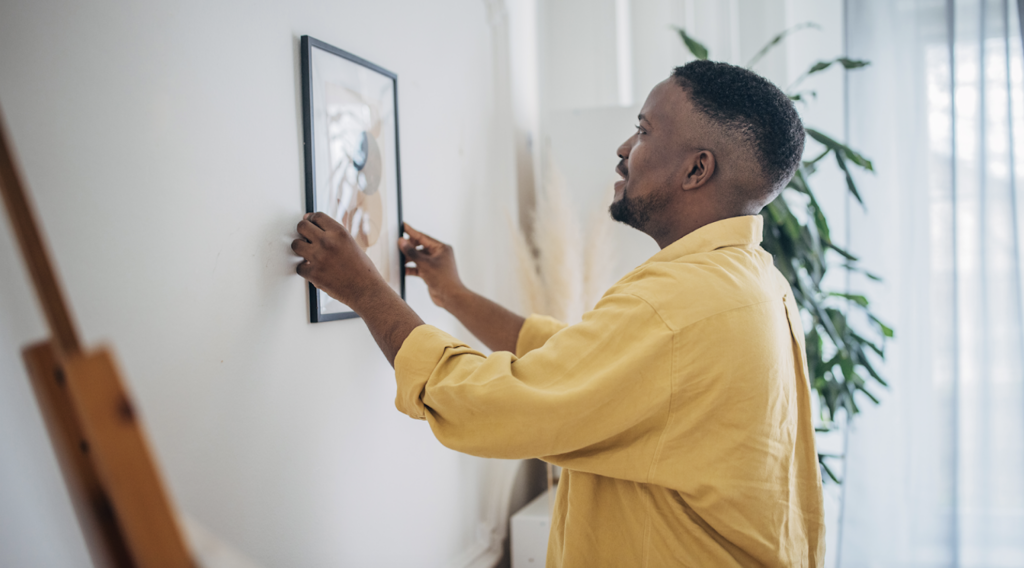 A man in a yellow shirt hanging a picture